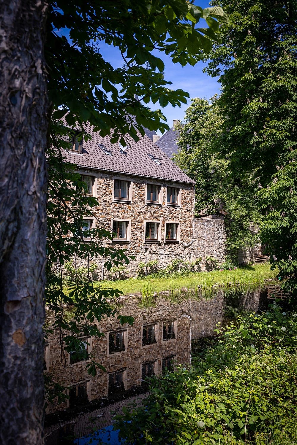 Bruchsteinhaus am Wassergraben, im Wasser spiegelt sich die Fassade