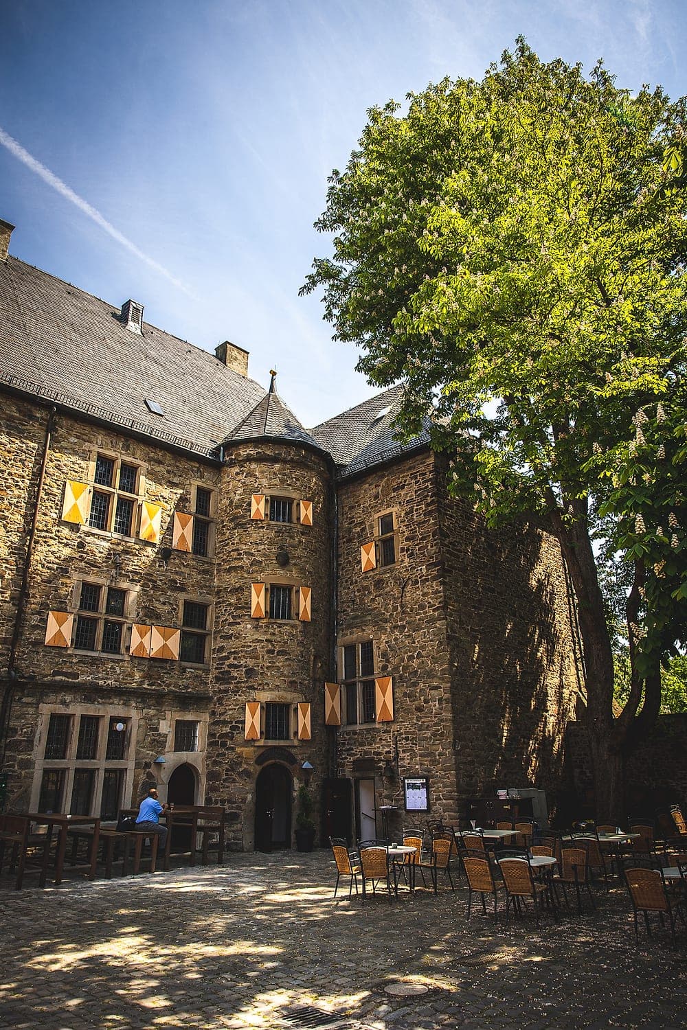 Der Innenhof von Haus Kemnade mit orange-weiß gerauteten Fensterläden und Bestuhlung unter der Kastanie